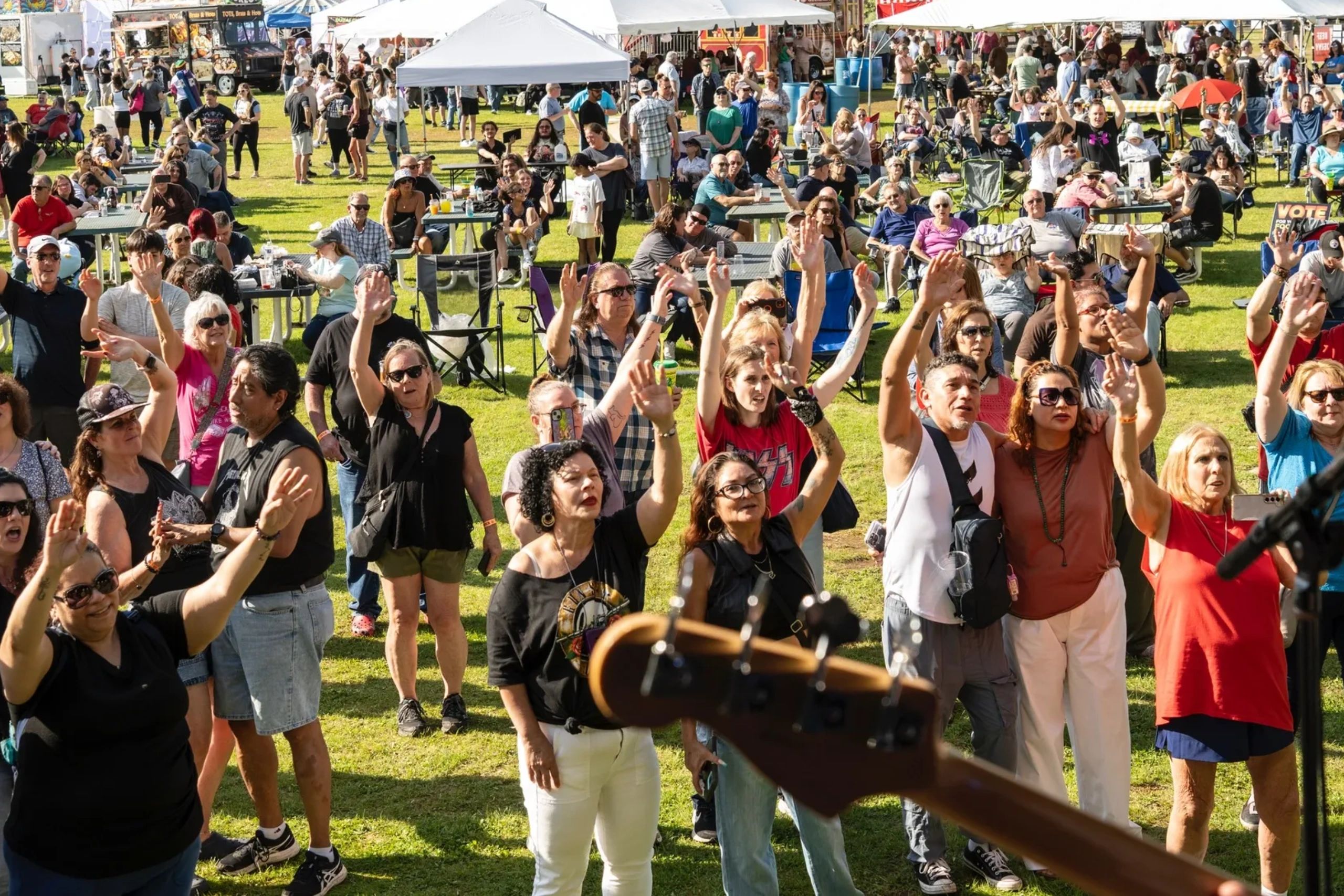 Hundreds of festival attendees on a sunny grass field